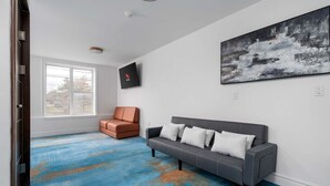 Une pièce avec un canapé gris, un fauteuil marron et un grand tableau abstrait accroché au mur.