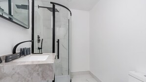 Une salle de bain moderne avec une douche à parois de verre, un lavabo en marbre et des toilettes.