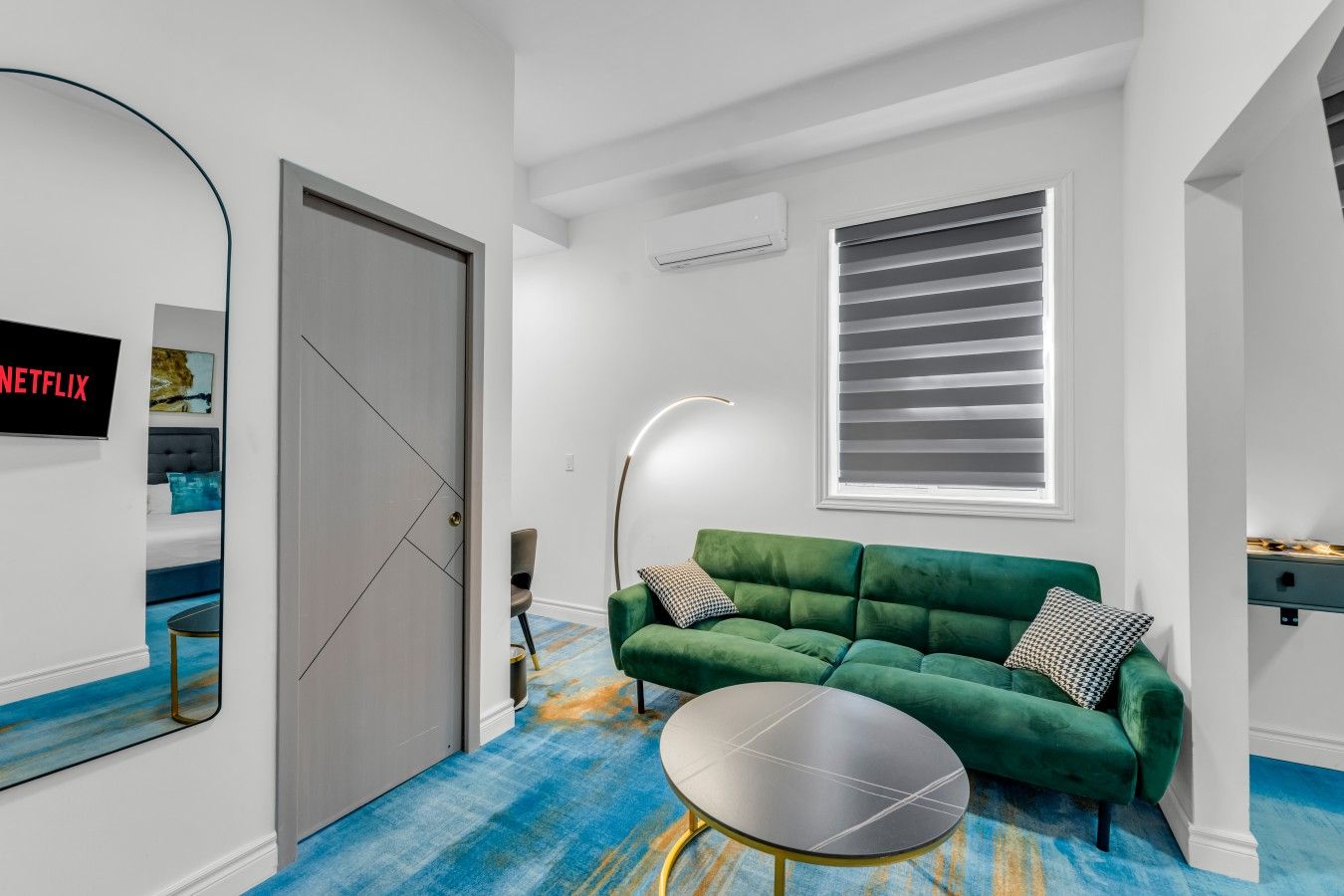 A modern living room with a green sofa, a round coffee table, and a large window with blinds.