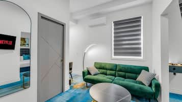 A modern living room with a green sofa, a round coffee table, and a large window with blinds.