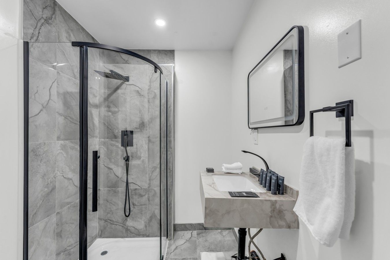Une salle de bain moderne dotée d’une douche à parois de verre, d’un meuble-lavabo recouvert de carreaux de marbre et d’un miroir fixé au mur.