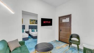 A hotel room with a bed, a green sofa, a small table, a door, and a wall-mounted TV displaying 'NETFLIX'.