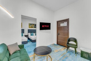 A hotel room with a bed, a green sofa, a small table, a door, and a wall-mounted TV displaying 'NETFLIX'.