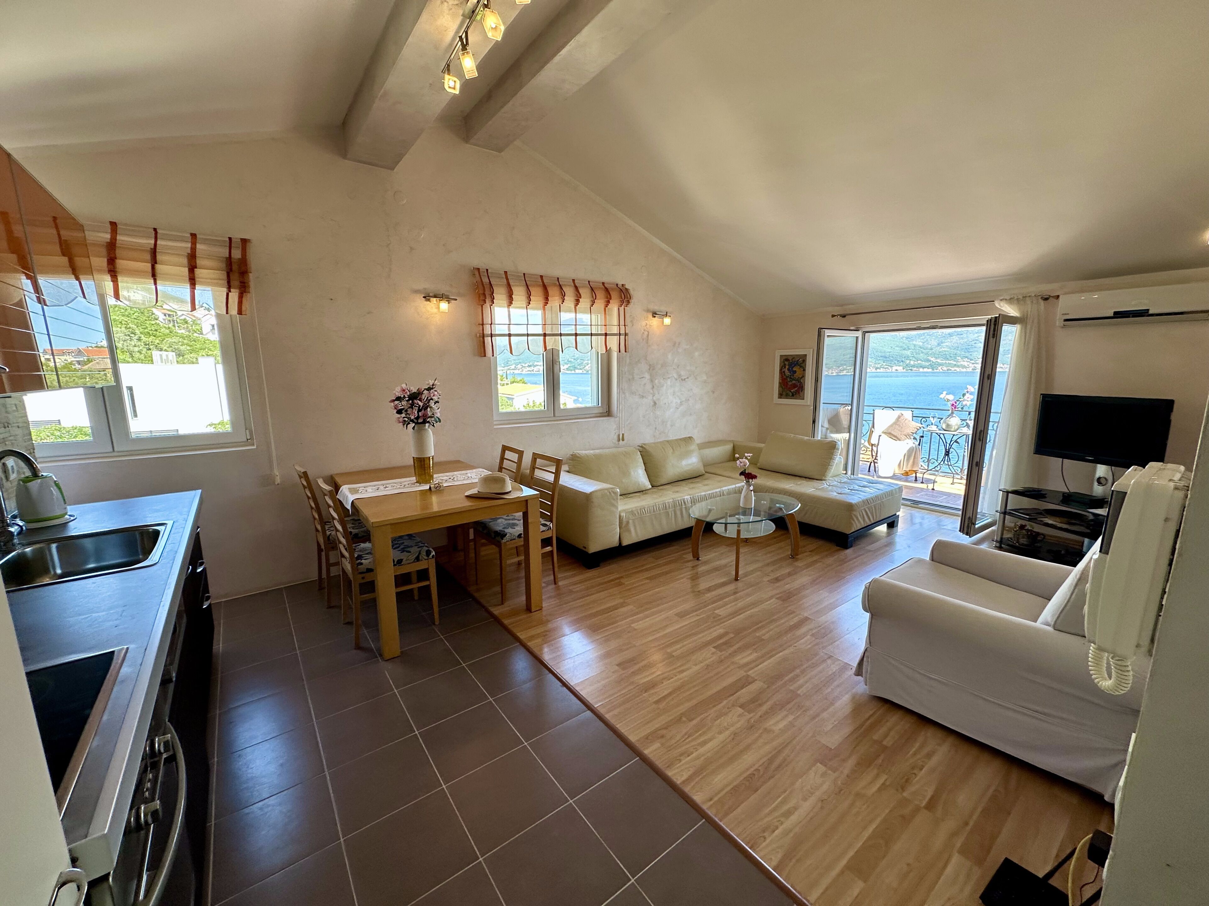 Una sala de estar con sofá, una mesa de comedor con sillas, televisor y una zona de cocina con fregadero.