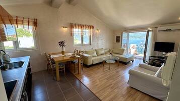 Una sala de estar con sofá, una mesa de comedor con sillas, televisor y una zona de cocina con fregadero.