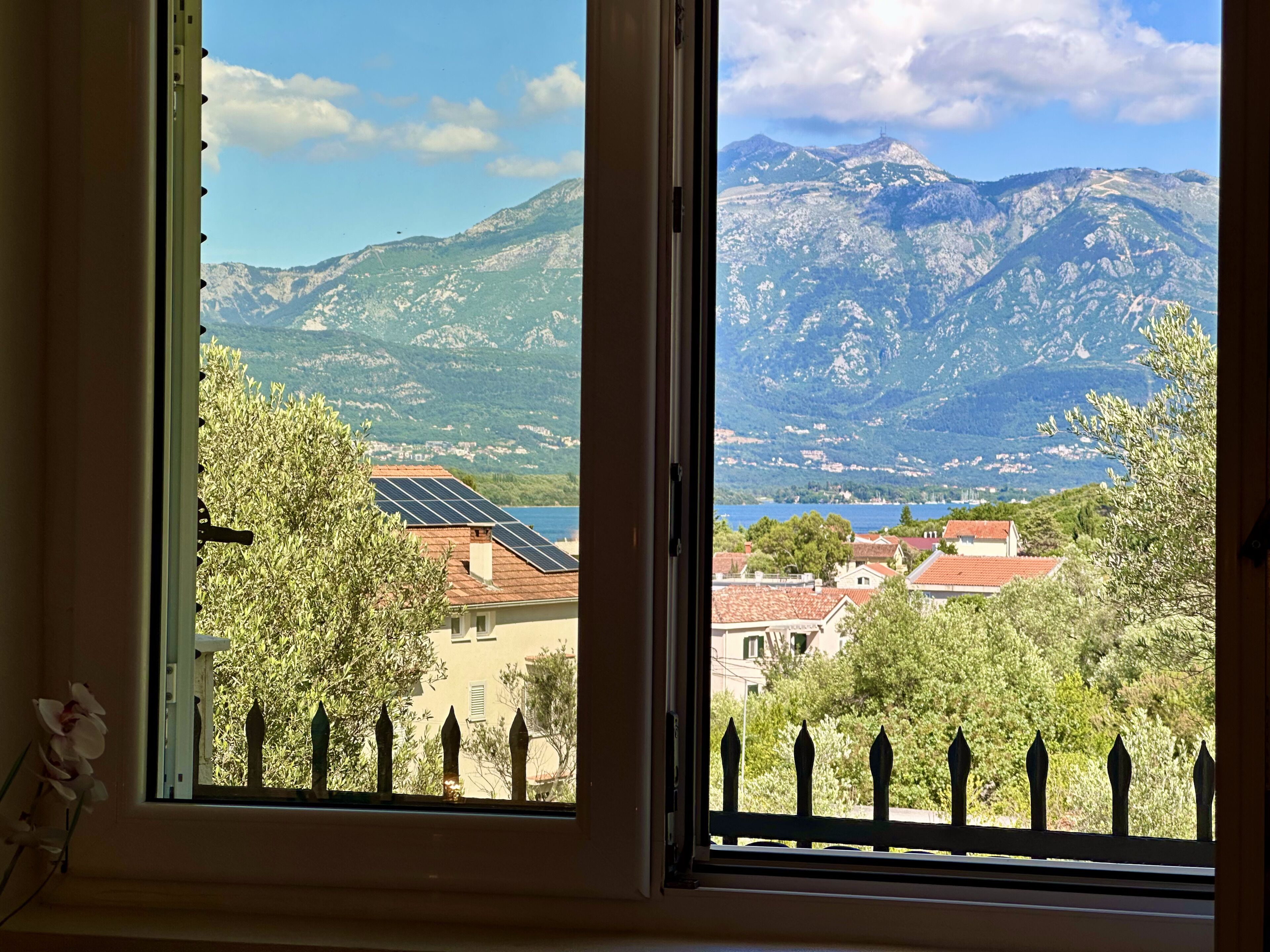 Vista desde una ventana de un paisaje montañoso con un lago, casas y paneles solares.