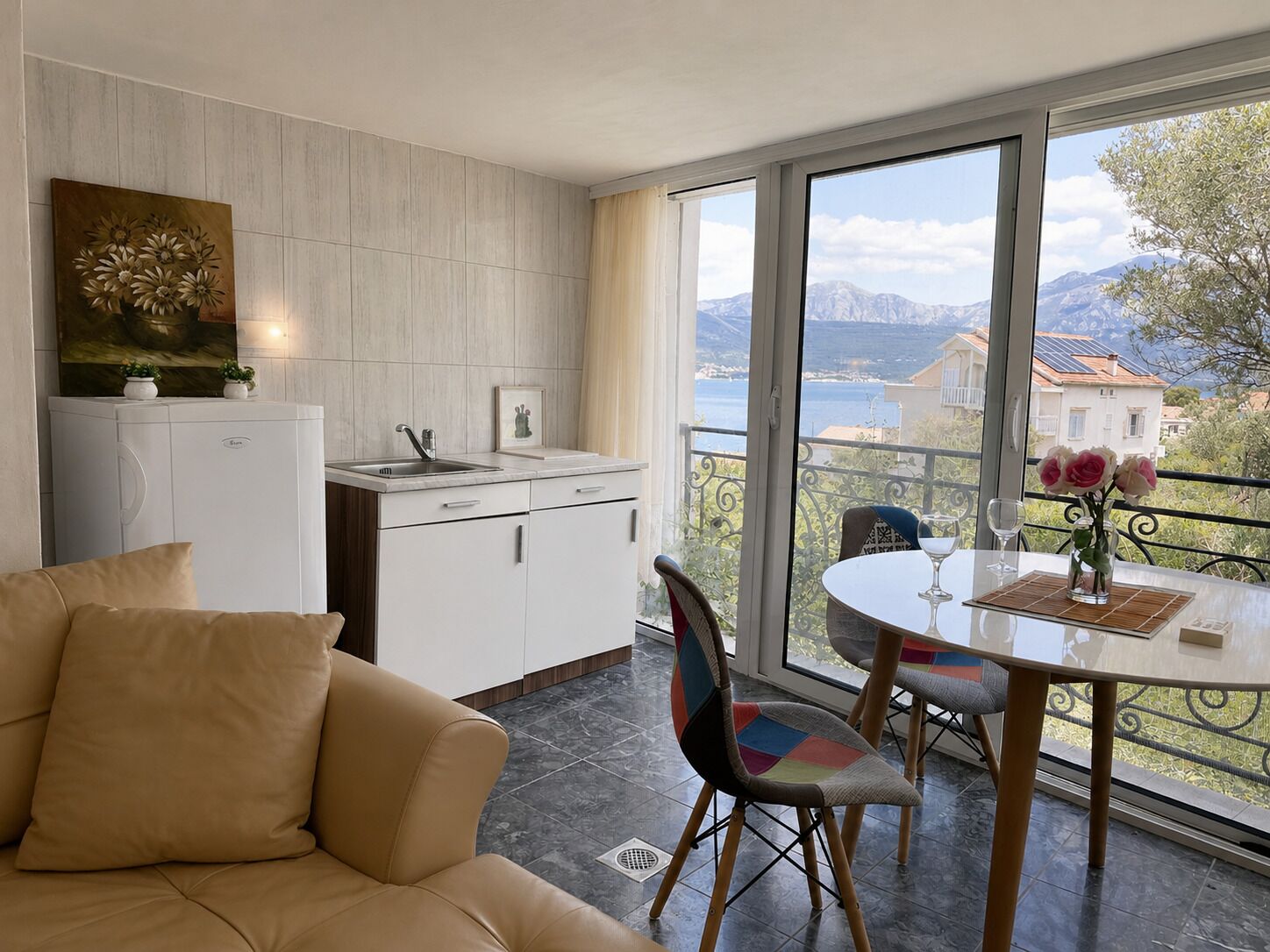 A modern kitchen with a view of the sea, a dining area with a table and chairs, and a sofa.