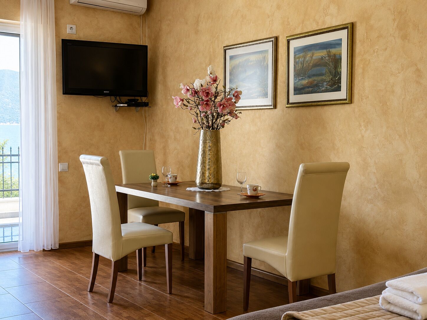 A dining area with a table, chairs, a vase with flowers, and two framed pictures on the wall.