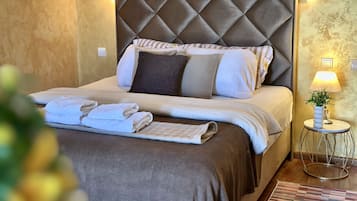 A neatly made bed with a quilted headboard, pillows, and a bedside table with a lamp and a small plant.