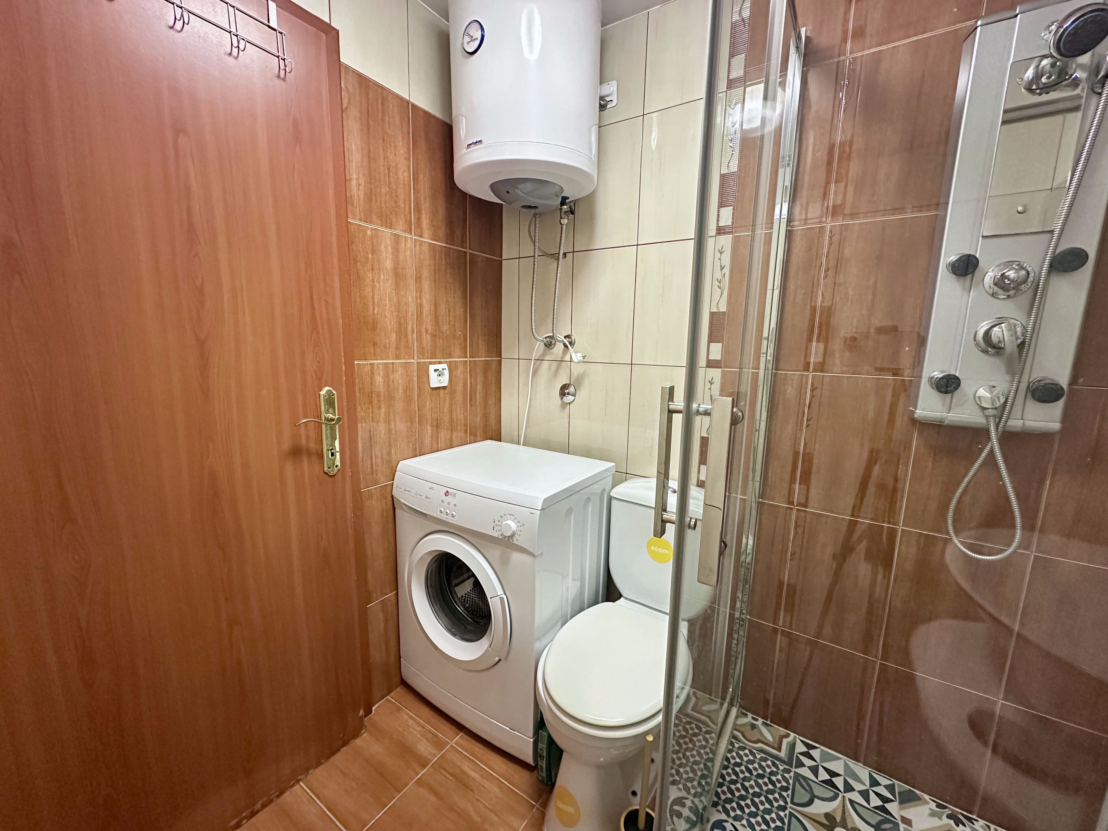 A compact bathroom with a washing machine, toilet, and shower.