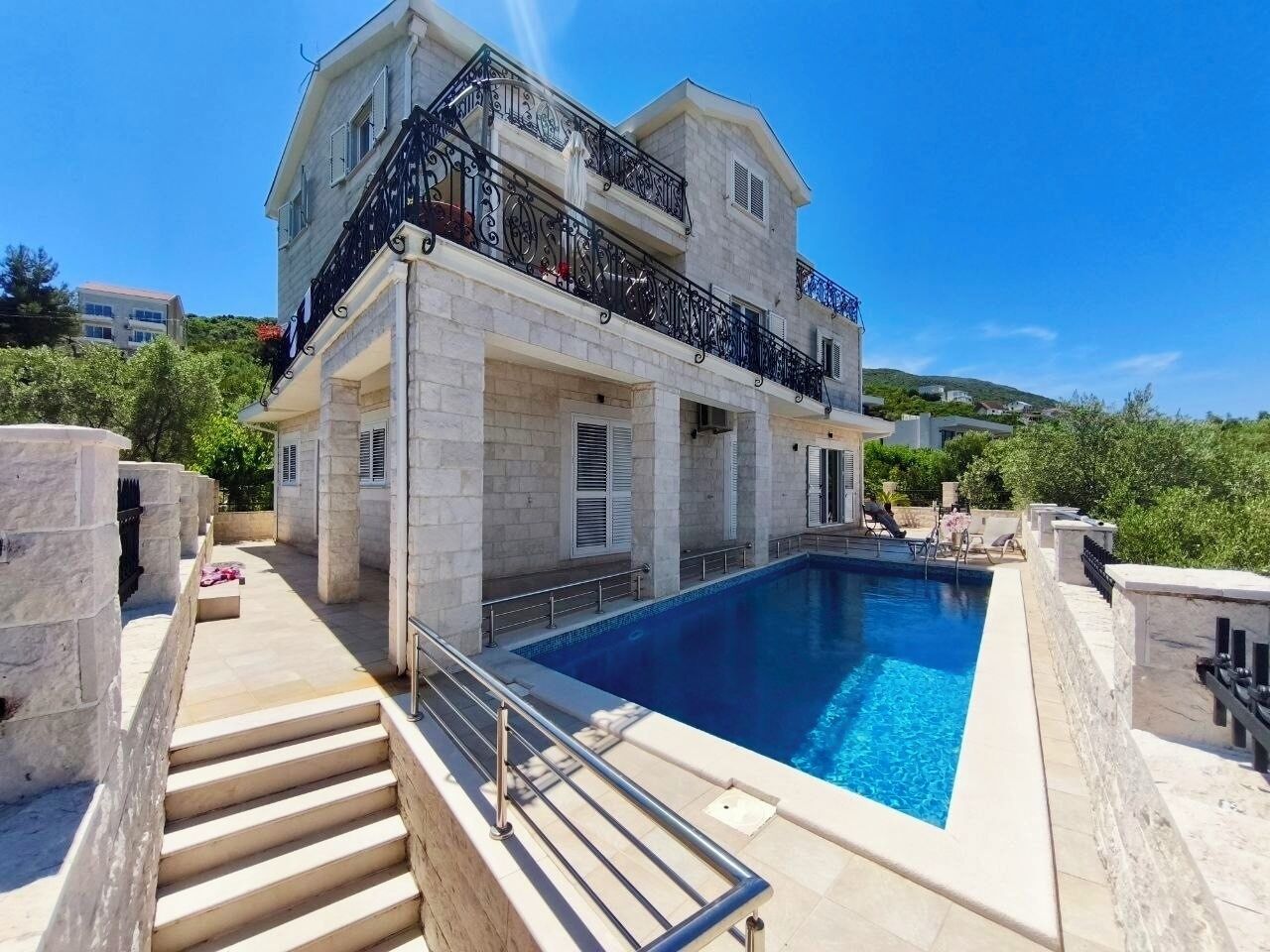 A two-story building with a swimming pool, stone steps, and a balcony with black railings.