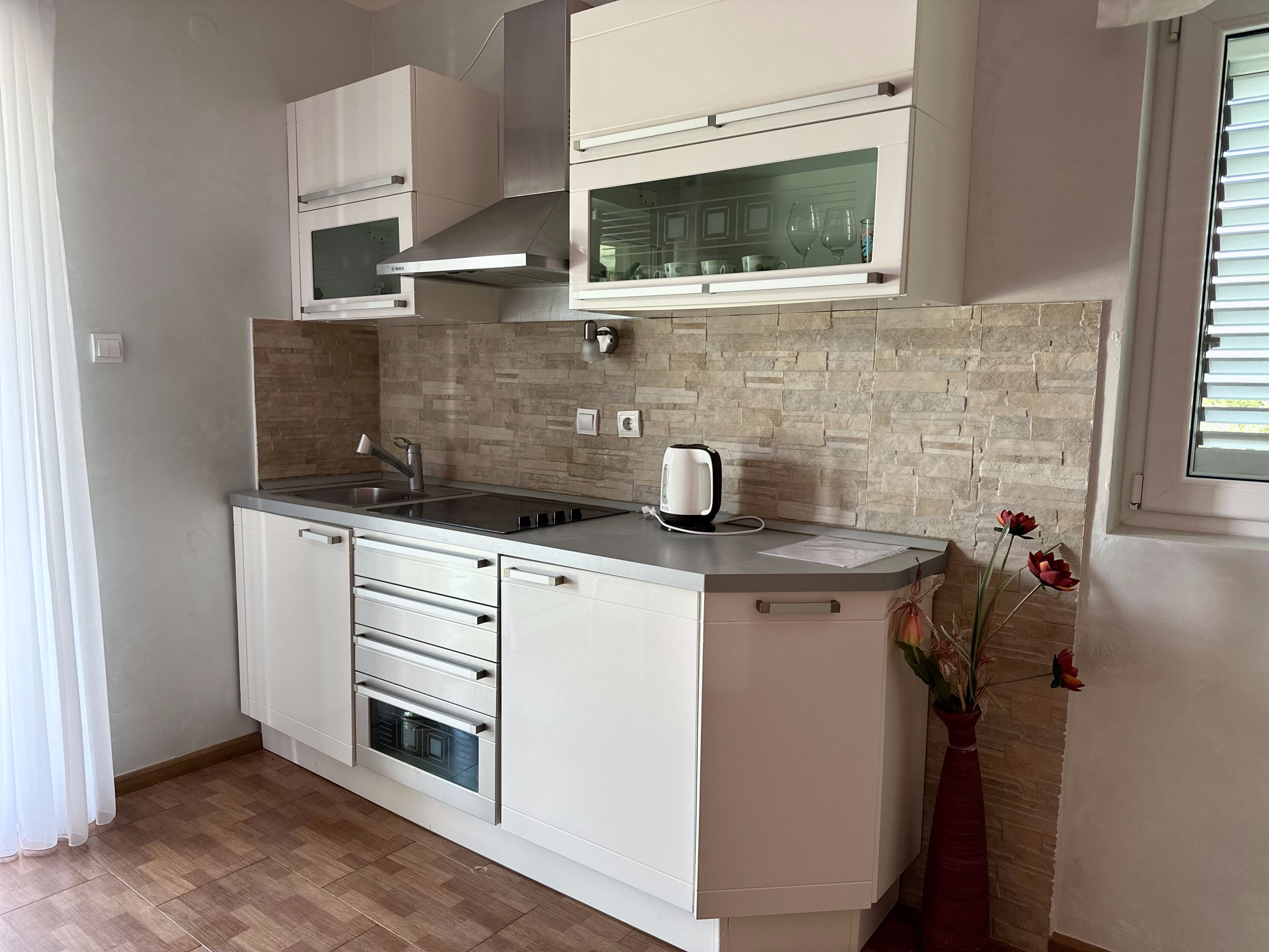 Une cuisine moderne avec des meubles blancs, un four encastré, un four à micro-ondes et une bouilloire.