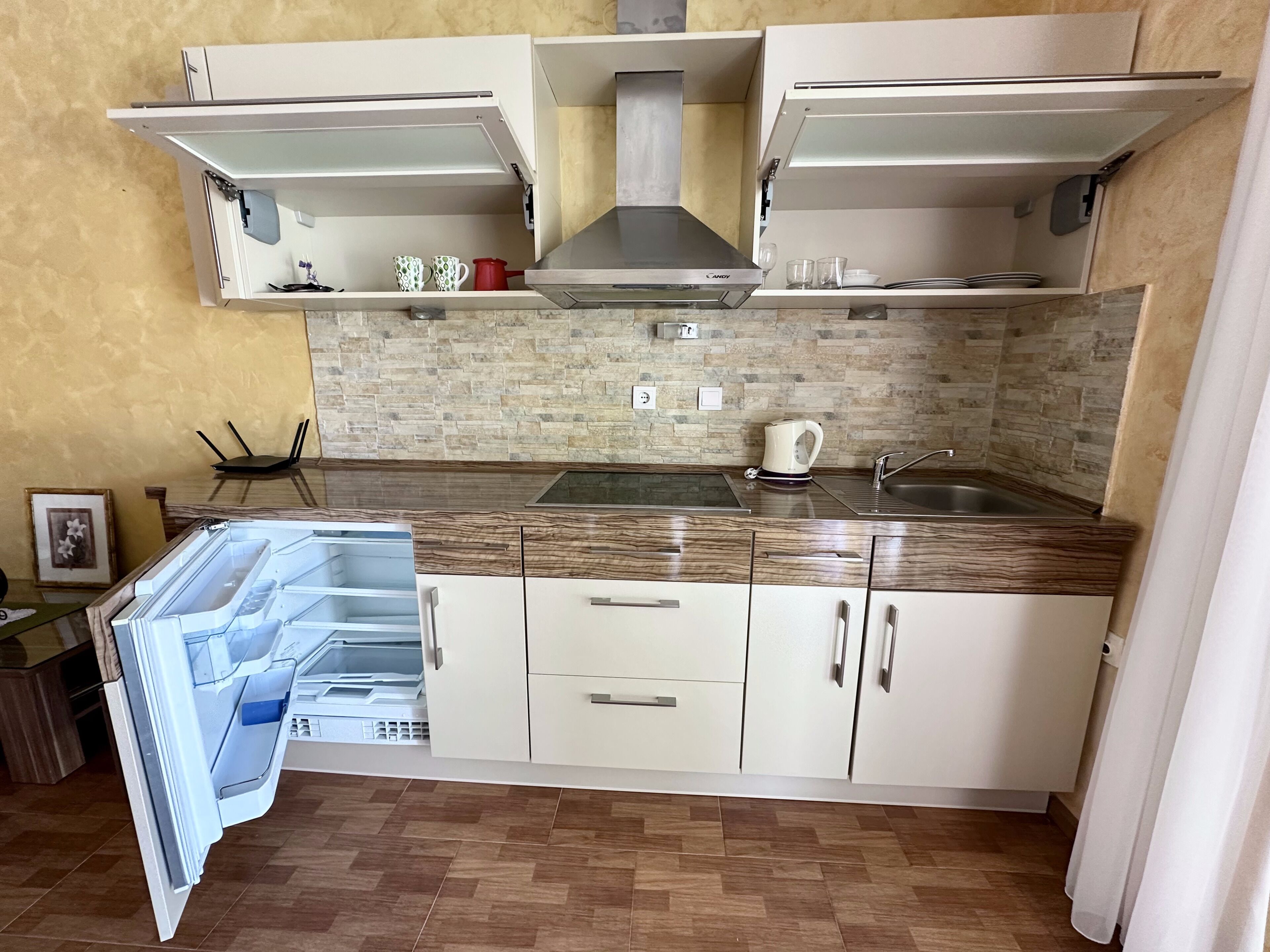 Una cucina con mobili bianchi, piano cottura integrato, bollitore e lavandino.