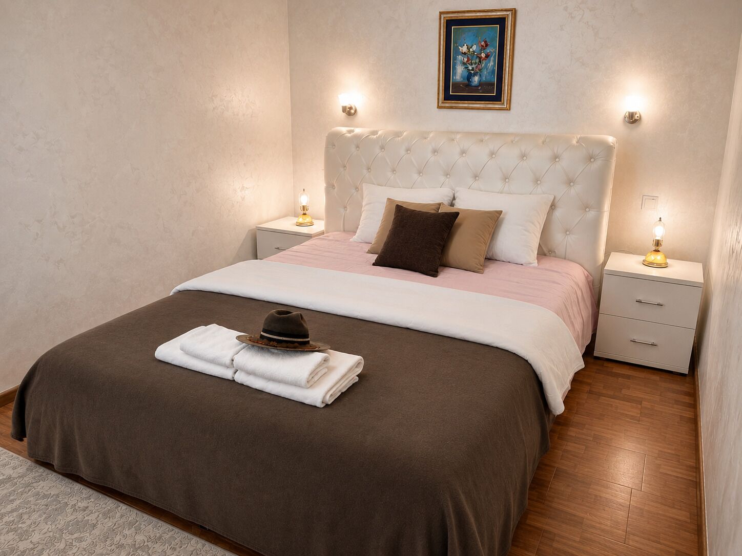 A neatly made bed with a brown and white bedspread, a white headboard, and two bedside tables with lamps.