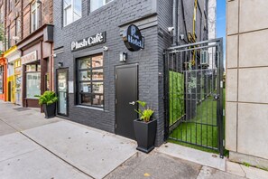 A building with a black exterior, a 'Push Café' sign, and a 'Blush Hotel' sign. There are two potted plants in front of the entrance.