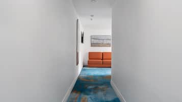 A narrow hallway with a blue carpet, white walls, and an orange sofa in the background.
