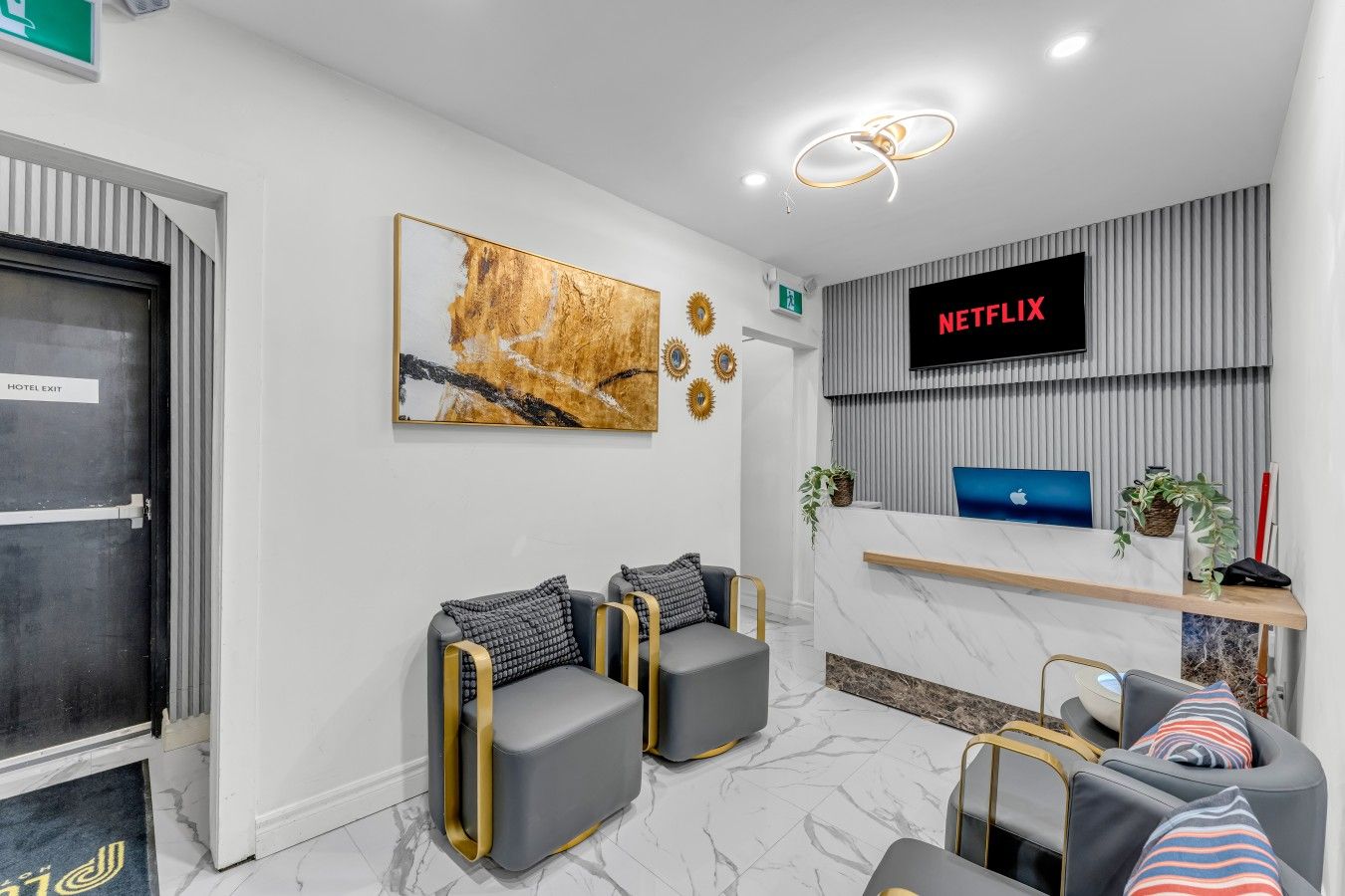 A hotel reception area with a Netflix screen, a reception desk, seating, and a door labeled 'HOTEL EXIT'.