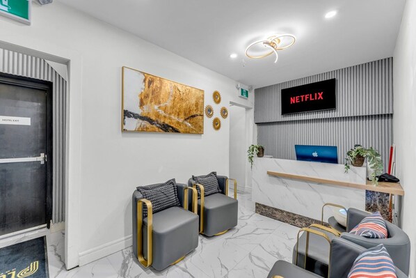 A hotel reception area with a Netflix screen, a reception desk, seating, and a door labeled 'HOTEL EXIT'.