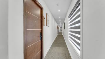 A corridor with a wooden door, a window with blinds, and a ceiling with recessed lighting.