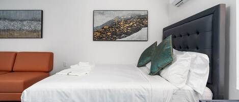 A modern hotel room with a bed, a sofa, and two paintings on the wall.