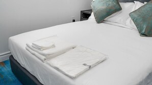 A neatly made bed with white linens, a folded towel, and two decorative pillows.