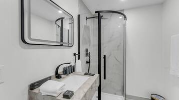 A modern bathroom with a glass-enclosed shower, a marble sink, and a large mirror.