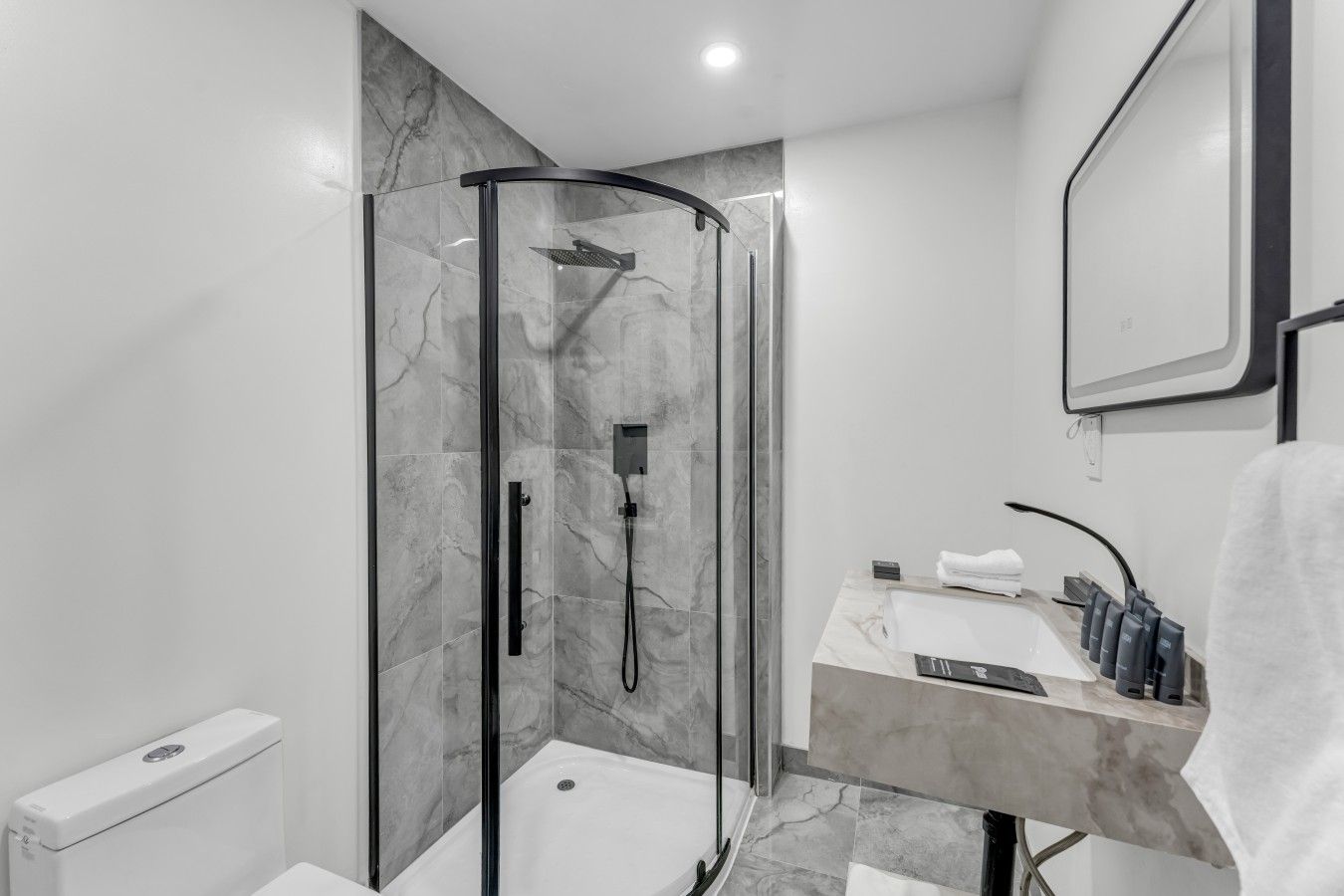 Une salle de bain moderne avec une douche à parois de verre, un lavabo en marbre et une serviette accrochée au mur.