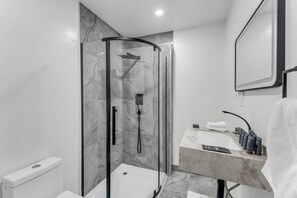 A modern bathroom with a glass-enclosed shower, a marble sink, and a towel hanging on the wall.