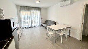 A modern, minimalist living space with a dining area, a sofa, and a kitchenette. - Bibione Apartment With Terrace and Pool (San Michele al Tagliamento)