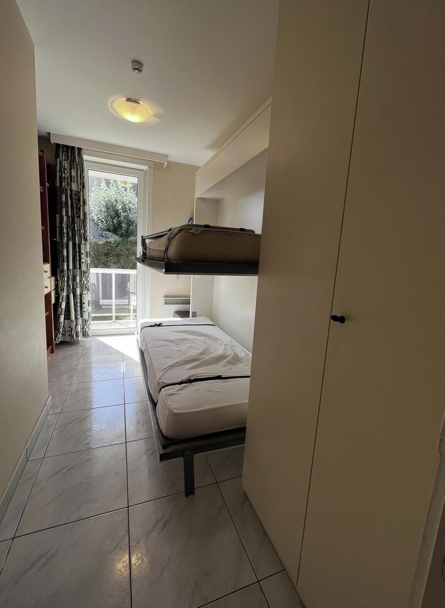 Una habitación pequeña con literas, una puerta y una ventana con cortinas.