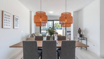 Un comedor con mesa de madera, sillas tapizadas en gris y lámparas colgantes de fibras anaranjadas.