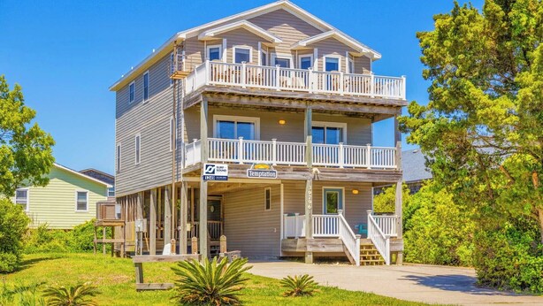 A two-story building with a balcony on the upper floor, a sign indicating a beach location, and a clear blue sky. - Soundside, Dog Friendly Home in Avon with Hot Tub (Avon)