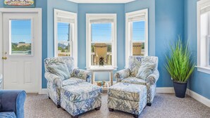 A room with a blue wall, three windows, two armchairs, a small table, and a potted plant. - Soundside, Dog Friendly Home in Avon with Hot Tub (Avon)