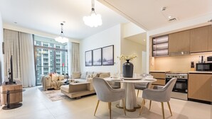 A modern living room with a dining area, a kitchen, and large windows. - Breathtaking Skyscraper Views 3BR, Just a Stone Throw from Burj Khalifa, Dubai Mall (Dubai)