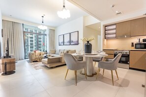 A modern living room with a dining area, a kitchen, and large windows. - Breathtaking Skyscraper Views 3BR, Just a Stone Throw from Burj Khalifa, Dubai Mall (Dubai)