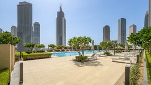 A modern urban setting with a swimming pool, lounge chairs, and high-rise buildings in the background. - Breathtaking Skyscraper Views 3BR, Just a Stone Throw from Burj Khalifa, Dubai Mall (Dubai)