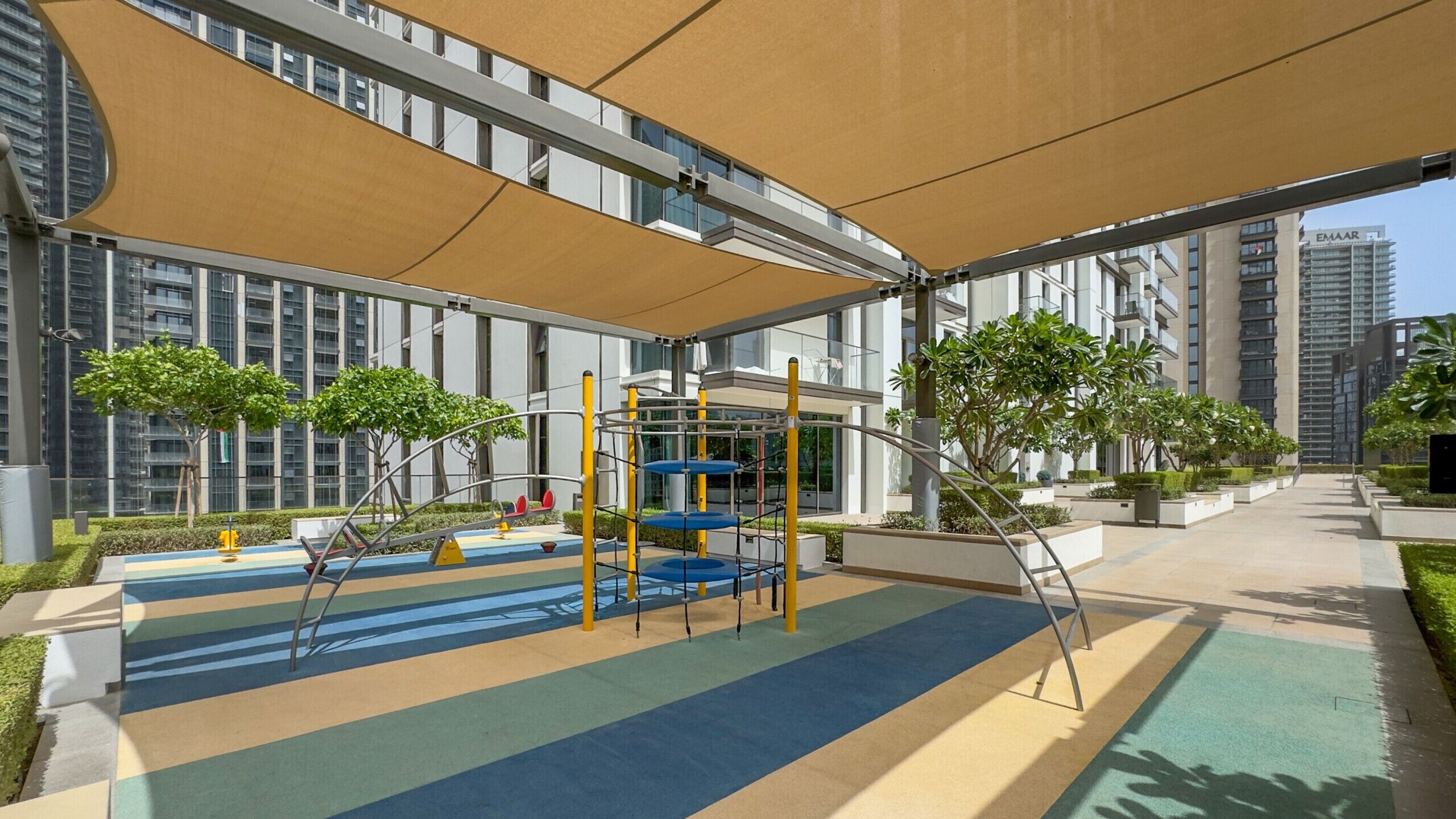 A playground with a climbing structure, surrounded by greenery and modern buildings.