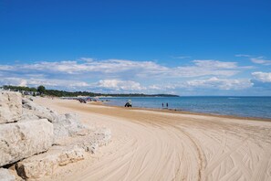 Ein Sandstrand mit einer Steinmauer, ruhigem Meer und blauem Himmel.