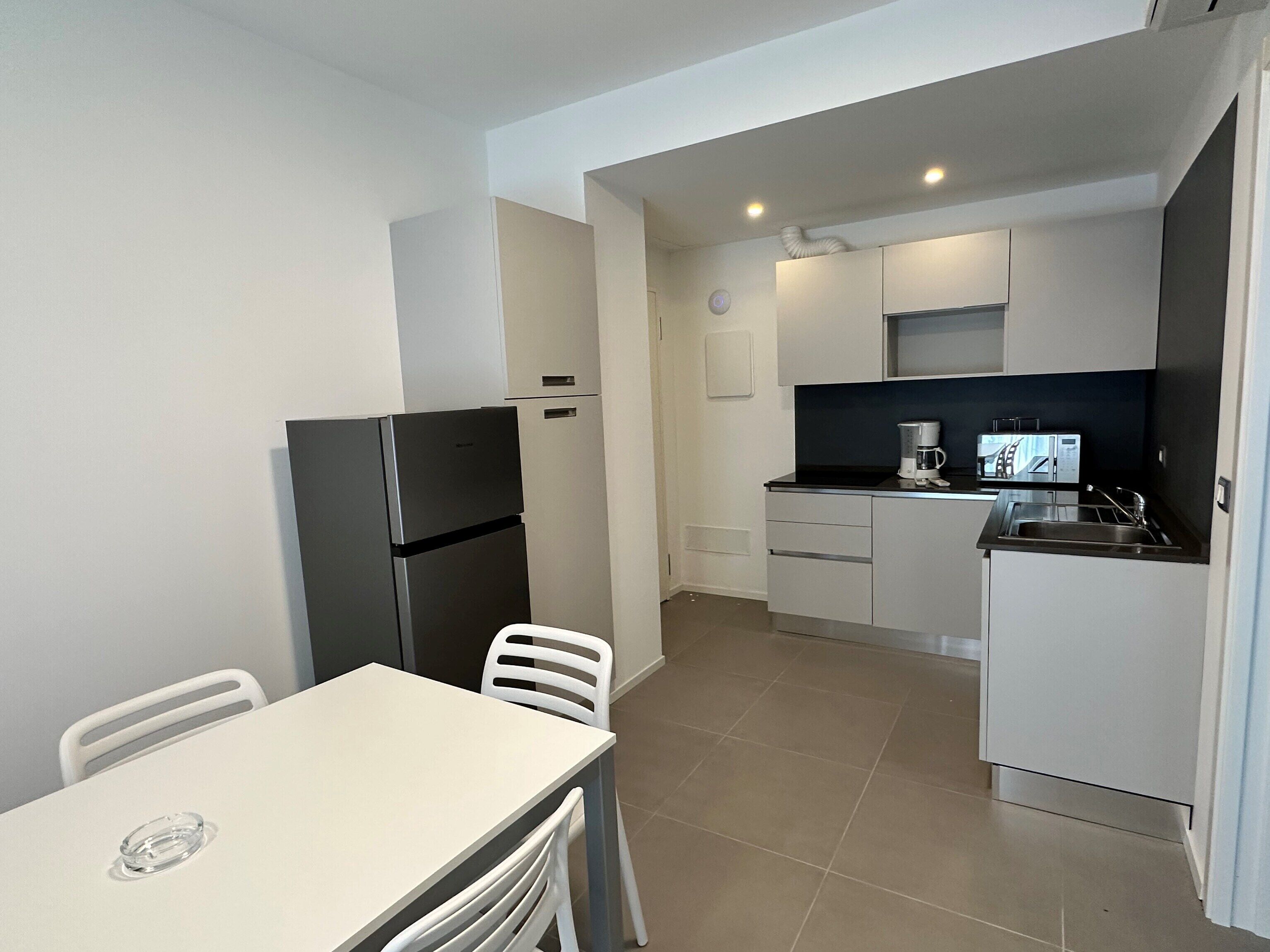 A compact kitchen with a refrigerator, a coffee maker, and a microwave. There is a dining table with chairs.