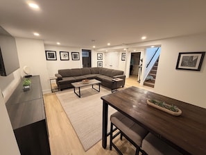 A modern living room with a sectional sofa, a dining table, and a kitchen in the background.