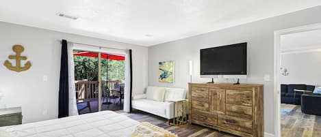 Un dormitorio con una cama, un aparador de madera, un televisor y un balcón con una sombrilla roja.