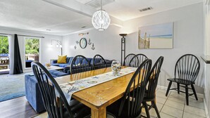 Zona pranzo con tavolo in legno, sedie nere, un lampadario e un'opera d'arte a tema spiaggia.