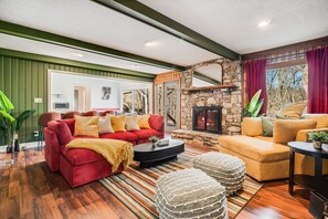 Una sala de estar con un sofá rojo, un sofá amarillo, una chimenea de piedra y un ventanal con cortinas rojas.