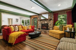 Ein Wohnzimmer mit Kamin aus Stein, roten und gelben Sofas, einem schwarzen Couchtisch und einem gestreiften Teppich.