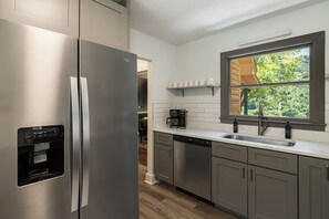 Eine moderne Küche mit Edelstahlgeräten, einem integrierten Wasserspender, einer Kaffeemaschine und einem Fenster mit Blick auf Grünflächen.