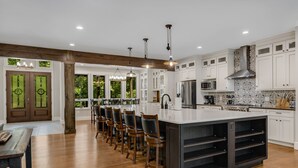 Una cocina moderna con armarios blancos, una isla grande con taburetes de bar y una campana extractora de acero inoxidable.