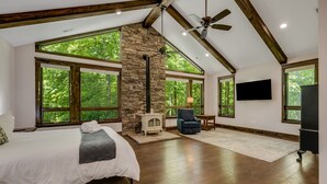 Un dormitorio con una cama grande, pared de piedra, chimenea, ventilador de techo y ventanas amplias.