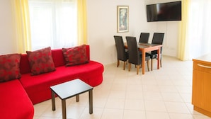 Un salon avec un canapé rouge, une petite table et un coin repas comprenant des chaises et un téléviseur.