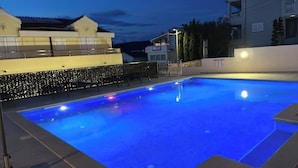 Une piscine dotée d’une terrasse carrelée, entourée d’un petit muret et d’une haie.