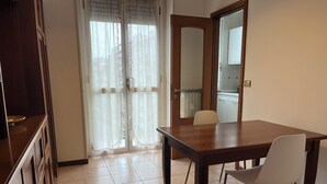 A dining area with a wooden table and white chairs, a kitchen visible through a glass door, and a tiled floor. - Three-room apartment de Angeli area (Milano)